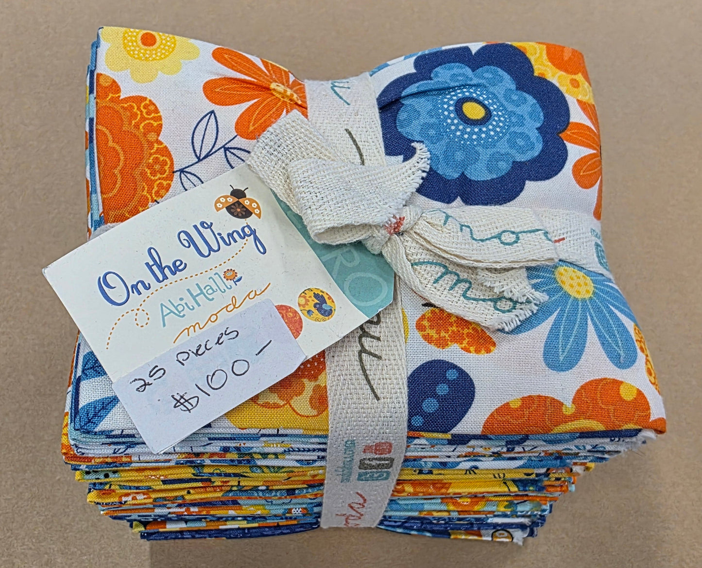 Stack of colorful fabric swatches with a 'On the Wing' label on a brown surface.